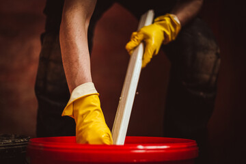 A worker washes a plastic part of a frame in a red bucket.