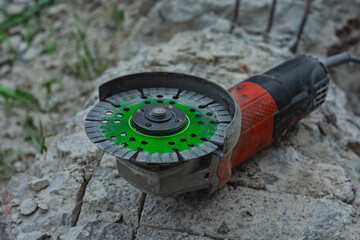 Close-up of an angle grinder with a green segmented diamond cutting disc placed on rough concrete...