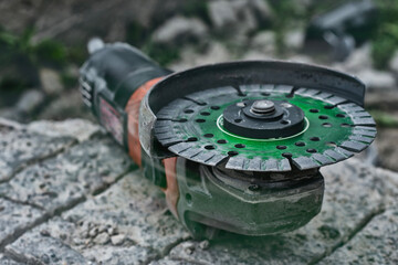 Close-up of an angle grinder with a green segmented diamond cutting disc placed on rough concrete...