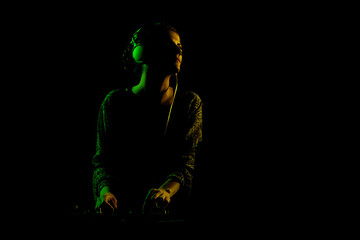 Female DJ with headphones on a mixer. Side lit silhouette of a girl playing techno music against...