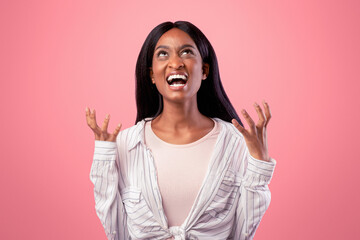 Portrait of angry young black woman screaming on pink studio background. African American lady...