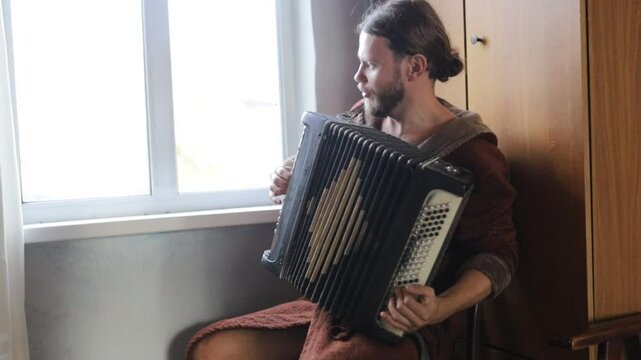 A long-haired man plays the accordion outdoors