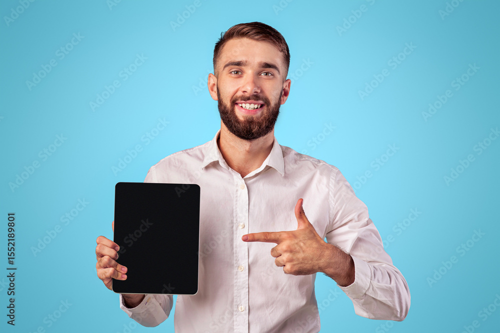 Aufkleber young businessman pointing at tablet with empty screen on blue studio background, mockup for applica