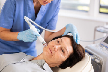 Aged female patient undergoing device-driven facial treatment using ion bubble pen attachment for...