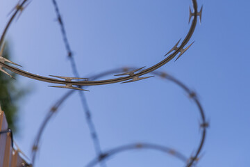  Close-Up of Razor Wire Spiral Against Clear Blue Sky – Symbol of Security, Control, or Border...