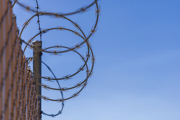 Coiled Barbed Wire on Chain-Link Fence with Blue Sky Background – Concept of Security and...