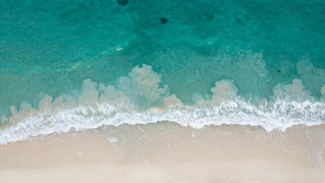 Top down view of ocean waves gently washing over sandy beach shoreline, seamless looping 4k time-lapse animation video background. Nature concept