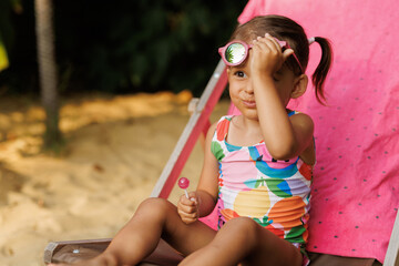 Funny cute girl on summer vacation. The child has fun near the pool. Cute baby girl in a colorful swimsuit and sunglasses is resting.