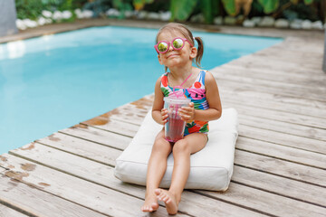 Funny cute girl on summer vacation. The child has fun near the pool. Cute baby girl in a colorful swimsuit and sunglasses is resting.