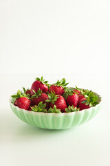 Fresh red strawberries in a green bowl on white table. Front view