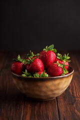 Fresh red strawberries in a rustic bowl on a dark wooden background. Front view