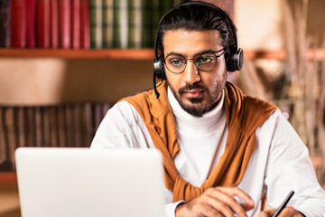 E-Learning Concept. Indian Male Student Studying Online At Laptop Learning Wearing Headset And...
