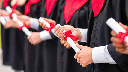 Hands of unrecognizable multiethnic group of male and female graduators wearing graduation robes...