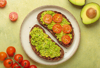 Two slices of whole rye bread are topped with mashed avocado, green peas, cherry tomatoes, and sesame seeds, a healthy and vibrant breakfast or snack option