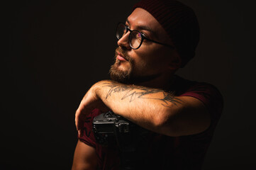 Confident male photographer with camera pointing left. Dramatic studio portrait on dark background,...
