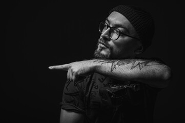 Moody black and white portrait of a tattooed male photographer holding a professional camera. Artistic low-key lighting highlights creative lifestyle concept