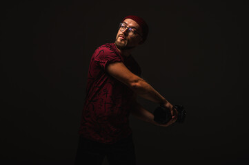 Stylish male photographer in red beanie and graphic tee posing in dramatic low key lighting, holding a camera against dark background. Urban creative vibe