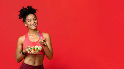 Healthy food concept. Happy African American Fitness Lady Eating Vegetable Salad, red studio...