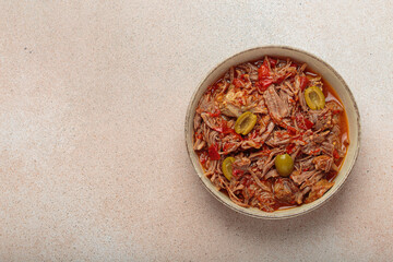 Ropa vieja, a traditional Cuban dish, is served with white rice, tomato sauce, and green olives on a plate from above on light beige background, copy space