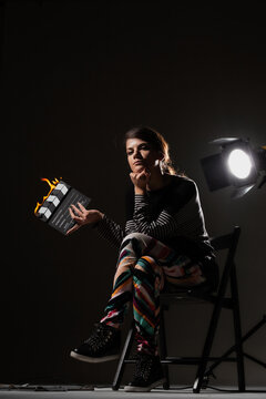 Female movie director on set with smoke background. Girl holding clapperboard on fire.