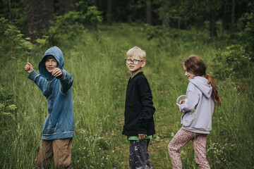 Three kids in casual hoodies enjoy a nature walk through tall grass, with one playfully posing,...