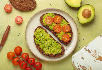 Slices of whole grain rye bread with mashed avocado, green peas and cherry tomatoes seasoned with black sesame seeds are served on a plate for a healthy breakfast or snack