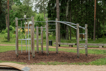 empty outdoor fitness playground with metal and wooden exercise equipment in forest park setting healthy lifestyle training area nature gym for bodyweight workout surrounded by trees and greenery