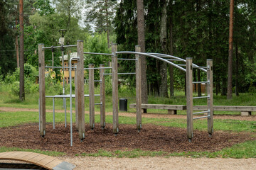 empty outdoor fitness playground with metal and wooden exercise equipment in forest park setting healthy lifestyle training area nature gym for bodyweight workout surrounded by trees and greenery