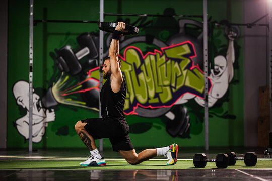 Athletic man performing a challenging overhead kettlebell lunge workout in a vibrant gym - Powered by Adobe