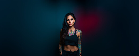 Confident woman with tattoos poses against a dark blue background, showcasing her unique style and body art during an urban photoshoot