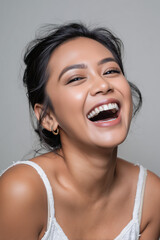 Joyful woman with dark hair and warm smile poses in soft light, showcasing vibrant laughter and natural beauty in an intimate setting