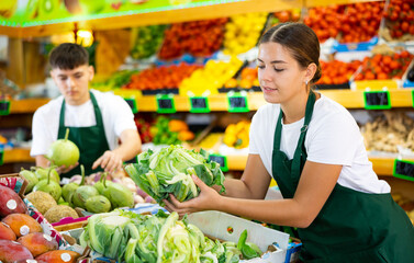 Portrait of young positive european woman working showing fresh cauliflower in grocery store