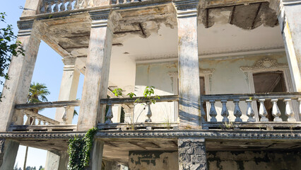 Old decaying building with classical columns and damaged balcony with visible vegetation and...