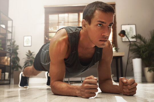 Sporty man doing plank exercise on floor at home