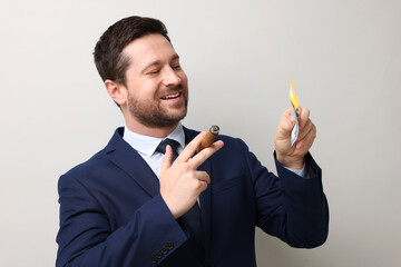 Greedy businessman with burning dollar banknote and cigar on light grey background