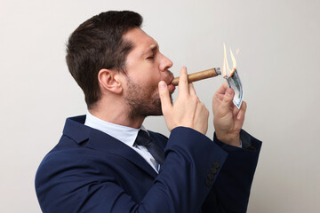 Greedy businessman lighting cigar with dollar banknote on light grey background