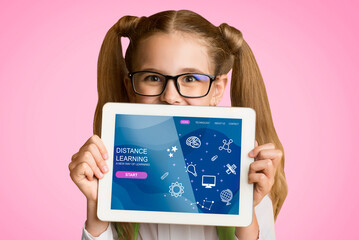 Funny schoolgirl showing tablet computer with distance learning class on screen, pink background....