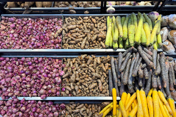 Assorted fresh vegetables on display at a local market, including turmeric, shallots, black carrots, yellow carrots and green carrots. Colorful and neatly arranged root vegetables for sale