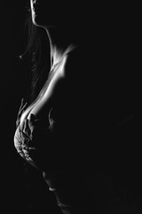 Artistic black and white portrait of a lady in dramatic lighting, holding her chest.