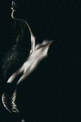 Low-key close-up portrait of a woman’s chest and lips in dramatic lighting, with dewy skin...