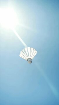 A white badminton shuttlecock is flying in the air. The shuttlecock is white and has a black stripe