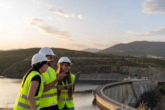 Engineers using laptop analyzing data at hydroelectric power plant dam