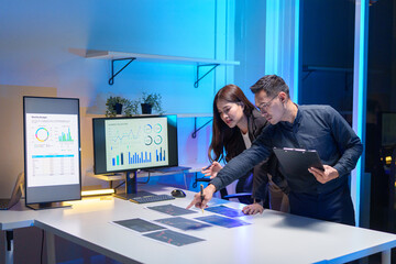 
Young Asian business team working late into the night in a well-lit office, collaborating on a project using laptops.