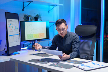 
Young Asian business team working late into the night in a well-lit office, collaborating on a project using laptops.