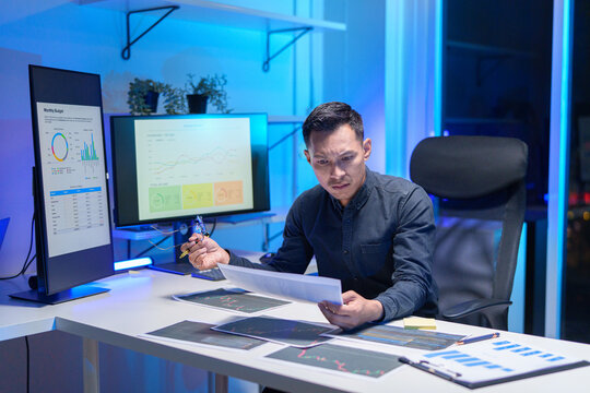 
Young Asian business team working late into the night in a well-lit office, collaborating on a project using laptops.