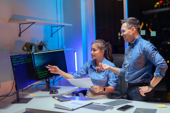 Two focused coders facing each other writing code in software development office while team of coders are developing artificial intelligence. Team of programmers innovating algorithm cod