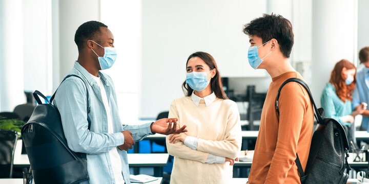 Healthcare, Education, Lifestyle And People Concept. Group of smiling diverse international students wearing protective medical masks and talking, standing in lecture hall at the university - Powered by Adobe