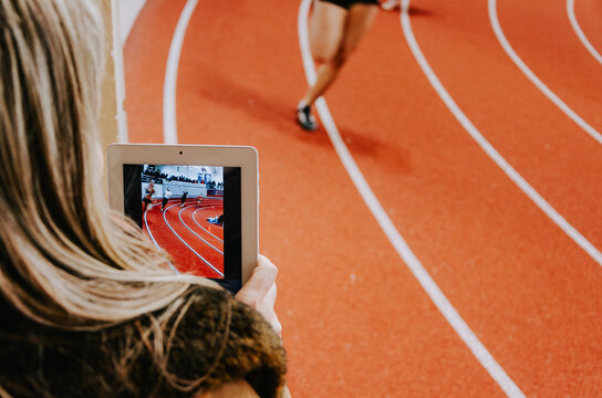 Athletic coach records sprinter’s performance using a tablet during training on the track field