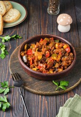 Ratatouille, vegetable stew of eggplant, zucchini, tomatoes and sweet pepper in a clay brown plate on a dark wooden background. Vegetable dishes.