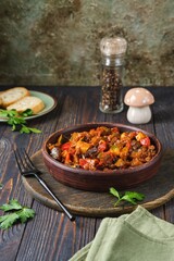 Ratatouille, vegetable stew of eggplant, zucchini, tomatoes and sweet pepper in a clay brown plate on a dark wooden background. Vegetable dishes.
